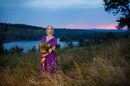 Girl model blonde in a lilac dress with a bouquet with a green forestの写真素材