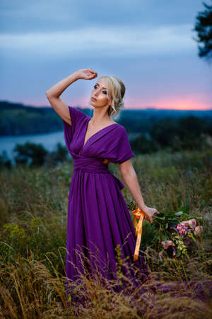 Girl model blonde in a lilac dress with a bouquet with a green forestの写真素材