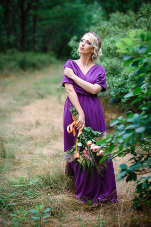 Girl model blonde in a lilac dress with a bouquet with a green forestの写真素材