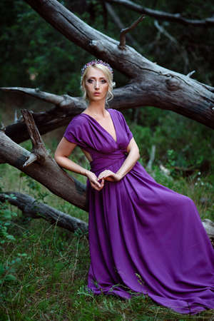 Girl model blonde in a lilac dress with a bouquet with a green forestの写真素材