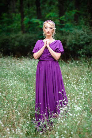 Girl model blonde in a lilac dress with a bouquet with a green forestの写真素材