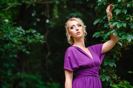 Girl model blonde in a lilac dress with a bouquet with a green forestの写真素材