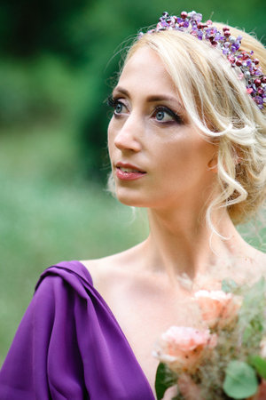Girl model blonde in a lilac dress with a bouquet with a green forestの写真素材