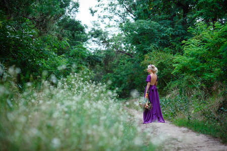 Girl model blonde in a lilac dress with a bouquet with a green forestの写真素材
