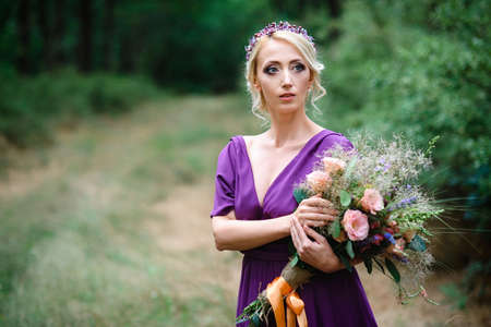 Girl model blonde in a lilac dress with a bouquet with a green forestの写真素材