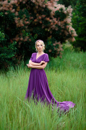 Girl model blonde in a lilac dress with a bouquet with a green forestの写真素材