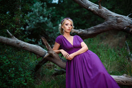 Girl model blonde in a lilac dress with a bouquet with a green forestの写真素材