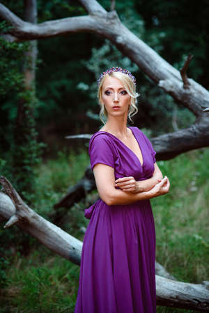 Girl model blonde in a lilac dress with a bouquet with a green forestの写真素材