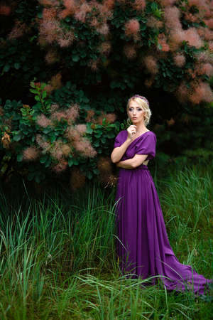 Girl model blonde in a lilac dress with a bouquet with a green forestの写真素材