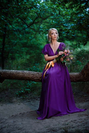 Girl model blonde in a lilac dress with a bouquet with a green forestの写真素材