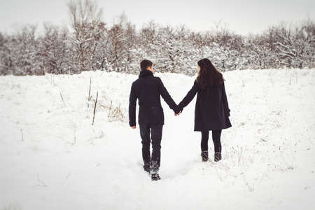 A guy and a girl in warm clothes and scarves on a walk in the snowy forest and in the fieldの写真素材