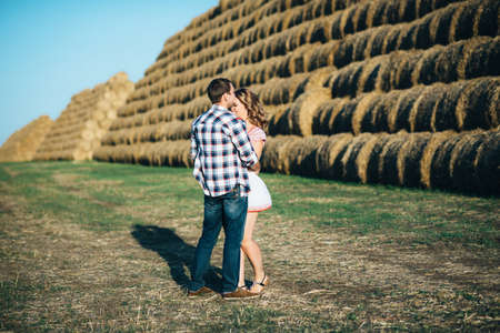 a guy with a girl on a summer walk in the field near round haystacksの写真素材