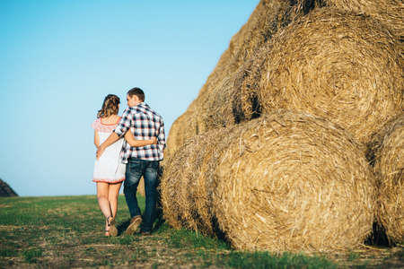 a guy with a girl on a summer walk in the field near round haystacksの写真素材