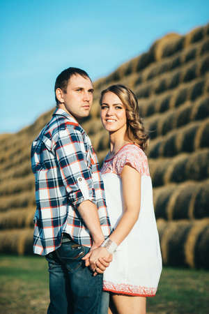a guy with a girl on a summer walk in the field near round haystacksの写真素材