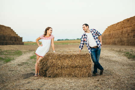a guy with a girl on a summer walk in the field near round haystacksの写真素材