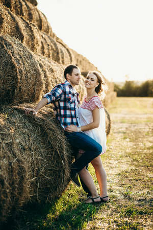 a guy with a girl on a summer walk in the field near round haystacksの写真素材