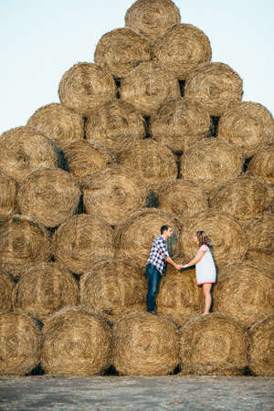 a guy with a girl on a summer walk in the field near round haystacksの写真素材
