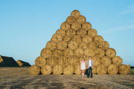 a guy with a girl on a summer walk in the field near round haystacksの写真素材