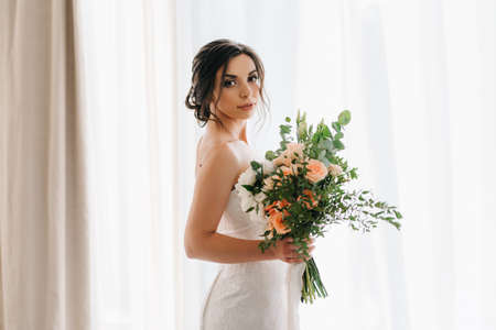 bride in a white dress with a bouquet in a hotel roomの写真素材