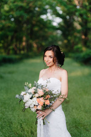 bride in a white dress with a large spring bouquet in a green forestの写真素材