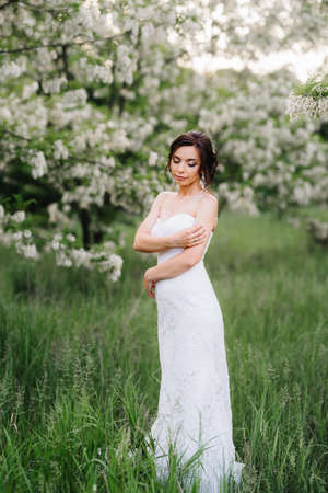 bride in a white dress with a large spring bouquet in a green forestの写真素材