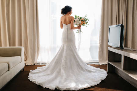 bride in a white dress with a bouquet in a hotel roomの写真素材