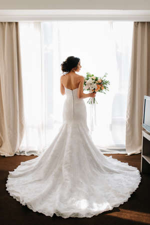 bride in a white dress with a bouquet in a hotel roomの写真素材