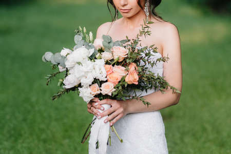 bride in a white dress with a large spring bouquet in a green forestの写真素材