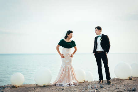 the groom in a brown suit and the bride in an ivory dress on the rocky seashoreの写真素材