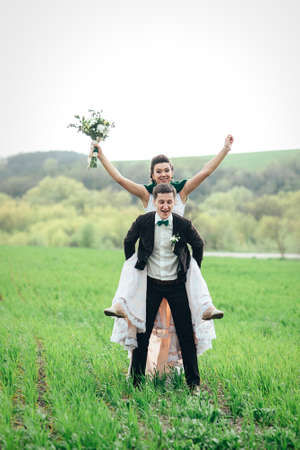 the groom in a brown suit and the bride in an ivory-colored dress on a green field receding into the distance against the skyの写真素材
