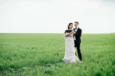 the groom in a brown suit and the bride in an ivory-colored dress on a green field receding into the distance against the skyの写真素材