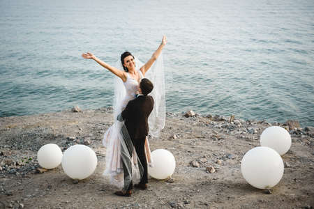 the groom in a brown suit and the bride in an ivory dress on the rocky seashoreの写真素材