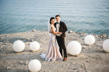 the groom in a brown suit and the bride in an ivory dress on the rocky seashoreの写真素材
