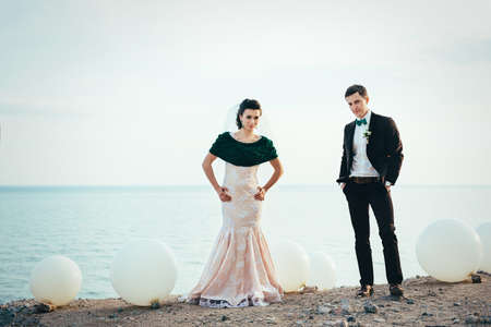 the groom in a brown suit and the bride in an ivory dress on the rocky seashoreの写真素材