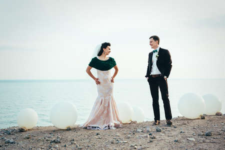 the groom in a brown suit and the bride in an ivory dress on the rocky seashoreの写真素材