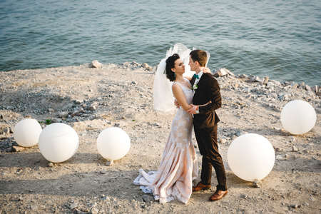 the groom in a brown suit and the bride in an ivory dress on the rocky seashoreの写真素材