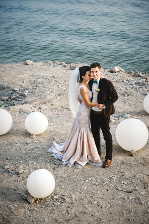 the groom in a brown suit and the bride in an ivory dress on the rocky seashoreの写真素材