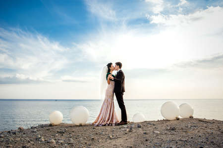 the groom in a brown suit and the bride in an ivory dress on the rocky seashoreの写真素材