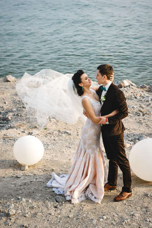the groom in a brown suit and the bride in an ivory dress on the rocky seashoreの写真素材