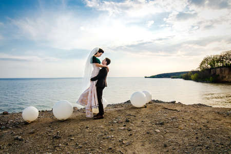 the groom in a brown suit and the bride in an ivory dress on the rocky seashoreの写真素材