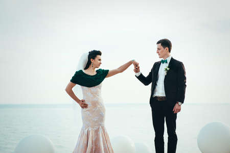 the groom in a brown suit and the bride in an ivory dress on the rocky seashoreの写真素材