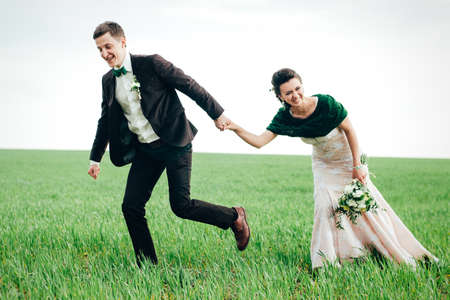 the groom in a brown suit and the bride in an ivory-colored dress on a green field receding into the distance against the skyの写真素材
