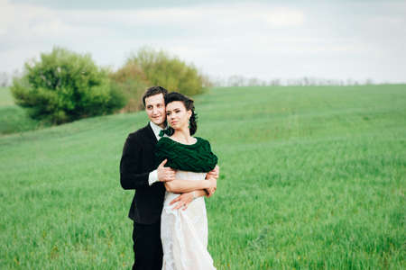 the groom in a brown suit and the bride in an ivory-colored dress on a green field receding into the distance against the skyの写真素材