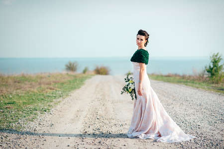 bride with a bouquet of flowers in an ivory dress and a knitted shawl on the road stretching into the distanceの写真素材
