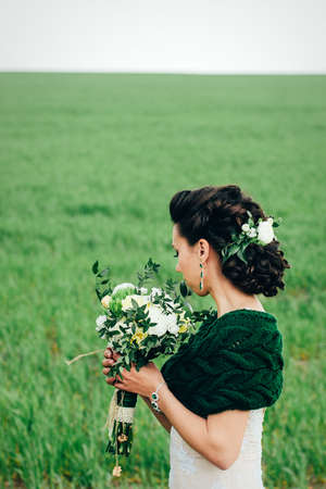 bride with a bouquet in an ivory dress and a knitted shawl on a green fieldの写真素材