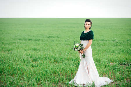 bride with a bouquet in an ivory dress and a knitted shawl on a green fieldの写真素材
