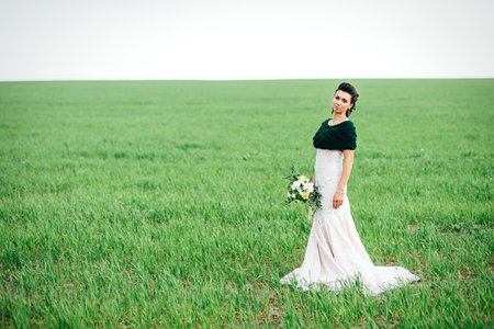 bride with a bouquet in an ivory dress and a knitted shawl on a green fieldの写真素材