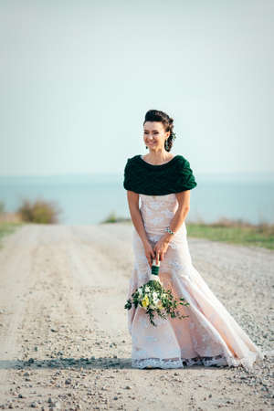 bride with a bouquet of flowers in an ivory dress and a knitted shawl on the road stretching into the distanceの写真素材