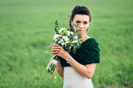 bride with a bouquet in an ivory dress and a knitted shawl on a green field