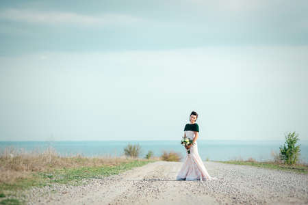 bride with a bouquet of flowers in an ivory dress and a knitted shawl on the road stretching into the distanceの写真素材